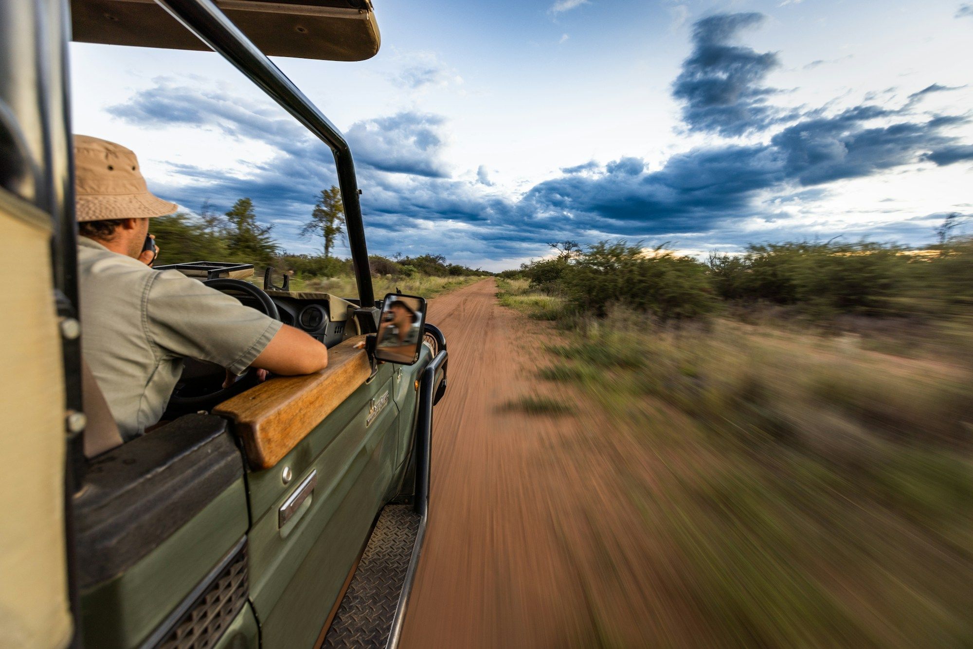 Een ranger rijdt een open safarivoertuig over een zandweg, de bush schiet voorbij
